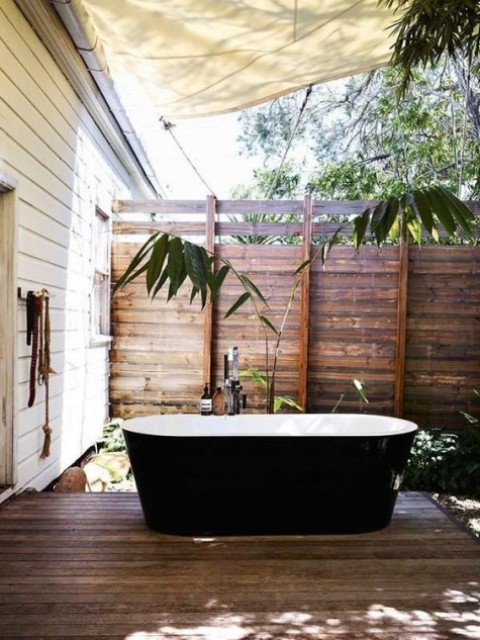 reclaimed wood privacy screens from all the sides, a black and white tub and some greenery growing here