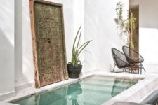 07 a minimalist pool space with boho touches, a wicker bench, an antique Asian door, metal chairs and potted plants
