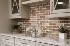 17 a small farmhouse kitchen with beige cabinets with a red brick backsplash and marble countertops