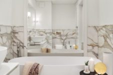 19 a modern refined bathroom done with white marble, an oval tub and a large mirror in a white frame