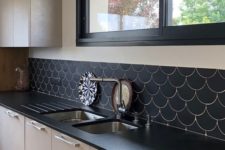 22 a monochromatic kitchen with black countertops, black frames and a black fishscale tile backsplash to make the space cohesive