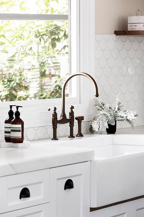 a fresh white kitchen with a white fishscale tile backsplash and white stone countertops looks airy