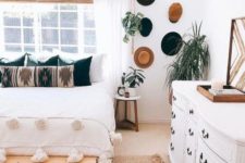 a black and white boho bedroom with hats on the wall, potted plants, a leather ottoman and a tassel blanket