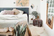a boho bedroom with an upholstered bed, layered rugs, potted plants, a wicker lamp and decorative plates on the wall