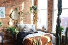 a boho bedroom with brick walls, potted succulents and cacti, colorful blankets and decorative plates on the wall