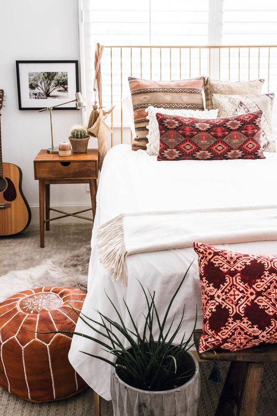 a boho bedroom with bright boho pillows, a leather ottoman, potted plants is stylish and very chic