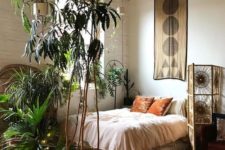 a boho bedroom with lots of potted plants, a woven screen, a tapestry over the bed is simple and cozy