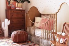 a boho bursery with a rich stained dresser, a vintage crib, a leather ottoman, a colorful rug and a polka dot wall