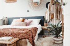 a boho chic bedroom with pastel pillows, printed blankets, layered rugs, a rattan bench and a wicker lamp