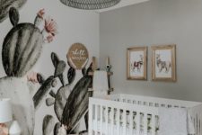 a boho desert nursery with a cactus wall, a pink tassel basket, a grey rattan lamp and llama artworks over the crib