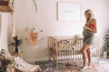 a boho nursery with a colorful printed rug, a beaded chandelier, natural wooden furniture and lots of greenery