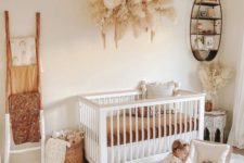 a boho nursery with a white crib, a ladder with colorful textiles, a Moroccan table and a pampas grass mobile