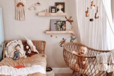 a boho nursery with wicker furniture, a large canopy with pompoms and a mobile, a gallery wall with macrame