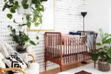 a bold mid-century and boho nursery with lots of potted greenery, a vintage bed, rattan furniture, gold touches and layered rugs