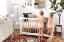 a bright boho nursery with a colorful rug, a potted plant, macrame and a beaded chandelier and neutral furniture