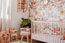 a bright boho nursery with a floral statement wall, wicker furniture and toys, a crib and potted plants plus a printed rug