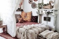 a chic boho bedroom in white, with a large mirror, bright printed pillows and blankets, a lace curtain and decorative plates