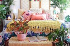 a colorful boho bedroom with a macrame headboard, colorful pillows and blankets, a woven bench and lots of plants