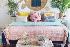 a colorful gypsy bedroom with bright pillows and blankets, a woven bench, potted plants and Moroccan lanterns