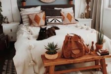a cute boho bedroom with printed pillows, potted greenery, a Moroccan lamp and a wooden artwork plus pompoms