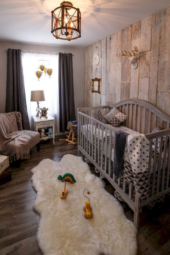 a farmhouse nursery with a reclaimed wooden wall, dark textiles, a grey crib, some gold touches here and there