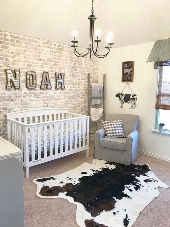 a farmhouse nursery with a whitewashed brick wall, vintage furniture, funny cow signs and a cowhide rug on the floor