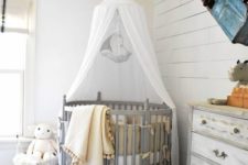 a farmhouse nursery with whitewashed grey furniture, a crib with a canopy, a vintage car on the wall and cute toys
