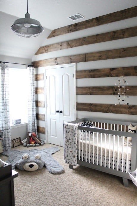 a farmhouse woodland nursery with a striped wall, a grey crib, a carpet on the floor, striped curtains and grey furniture
