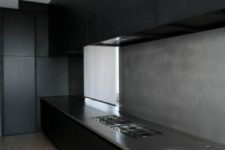 a minimalist black kitchen with a concrete backsplash and countertops for more interest