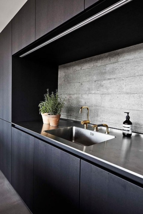 a minimalist dark kitchen with a raw concrete backsplash and a metal countertop that adds texture