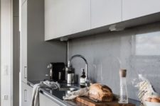 a minimalist light grey kitchen with a concrete backsplash and a glass cover to avoid splashes