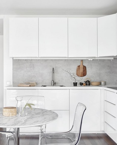 a minimalist white kitchen gets texture and interest with a concrete backsplash and a marble kitchen table