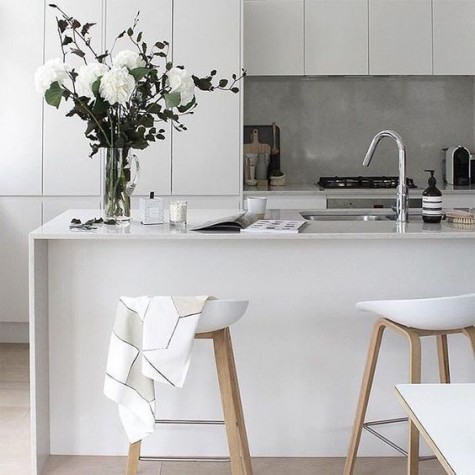 a minimalist white kitchen with a concrete backsplash that adds texture to the space and a sleek stone countertop