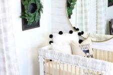 a modern farmhouse nursery with white plank walls, a neutral wooden crib, a gold chandelier and a greenery wreath