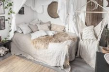a neutral boho bedorom with a bed with lots of pillows and linen bedding, a canopy, a hanging chair, a woven tassel chandelier and layered rugs