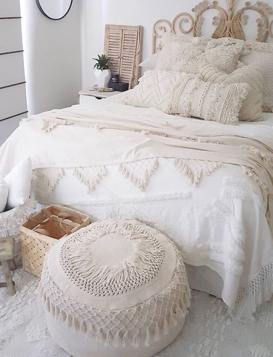 a neutral boho bedroom with neutral bedding, Moroccan pillows and a blanket, a Moroccan pouf and layered rugs