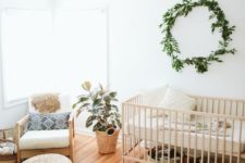 a neutral boho nursery with a greenery wreath, a bright rug, jute ottomans, printed pillows and a potted plant