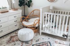 a neutral boho nursery with a printed rug, white furniture, a rattan chair, some baskets and wicker trays