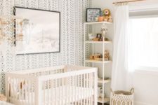 a neutral boho nursery with a printed wall, a printed rug, a leather ottoman, a white crib and a woven basket