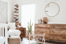a neutral boho nursery with a rattan lamp, a wooden dresser, layered rugs, a leather chair and a wooden shelf in the corner