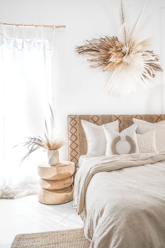 a neutral boho space with an embroidered bed, a jute rug, linen bedding, a cutout wooden side table and dried fronds