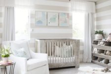 a neutral farmhouse nursery with striped walls, a wooden furniture, a watercolor gallery wall and potted greenery
