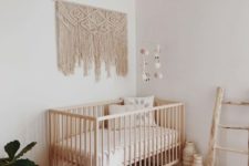 a simple boho nursery with a colorful rug, a macrame hanging, a wicker chandelier, potted greenery and wicker bottles and jars