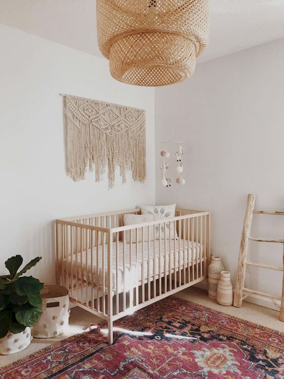 a simple boho nursery with a colorful rug, a macrame hanging, a wicker chandelier, potted greenery and wicker bottles and jars
