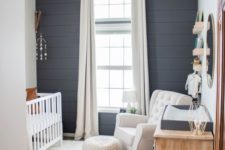 a stylish farmhouse nursery with a grey plank wall, white furniture, layered rugs and a large window for more light