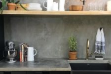 black industrial cabinets, wooden shelves that contrast and a concrete backsplash and countertops