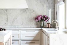 13 a refined glam kitchen done in neutrals, with a large hood, wooden beams and a white marble backsplash and countertops