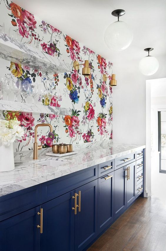 a navy kitchen with gold touches, white stone countertops and a colorful floral backsplash that makes a statement