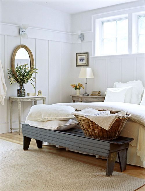 a French farmhouse bedroom in white, with vintage furniture of wood, elegant decor and some greenery