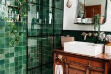 a beautiful bathroom with a green tile shower space, a vintage stained vanity, baskets, a mirror with a shelf